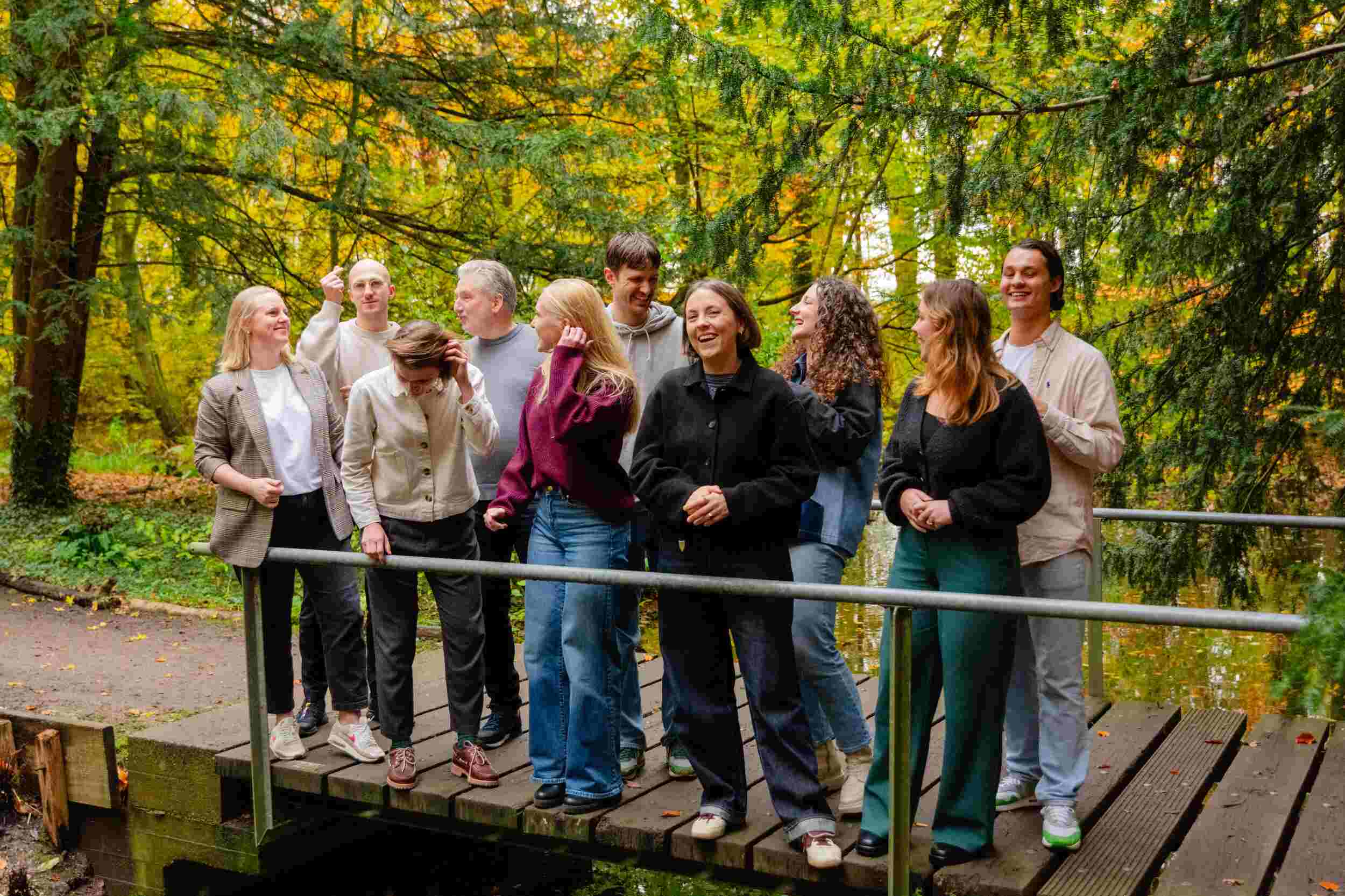 Een vrolijk team van Over/Nieuw staat op een brug in het bos